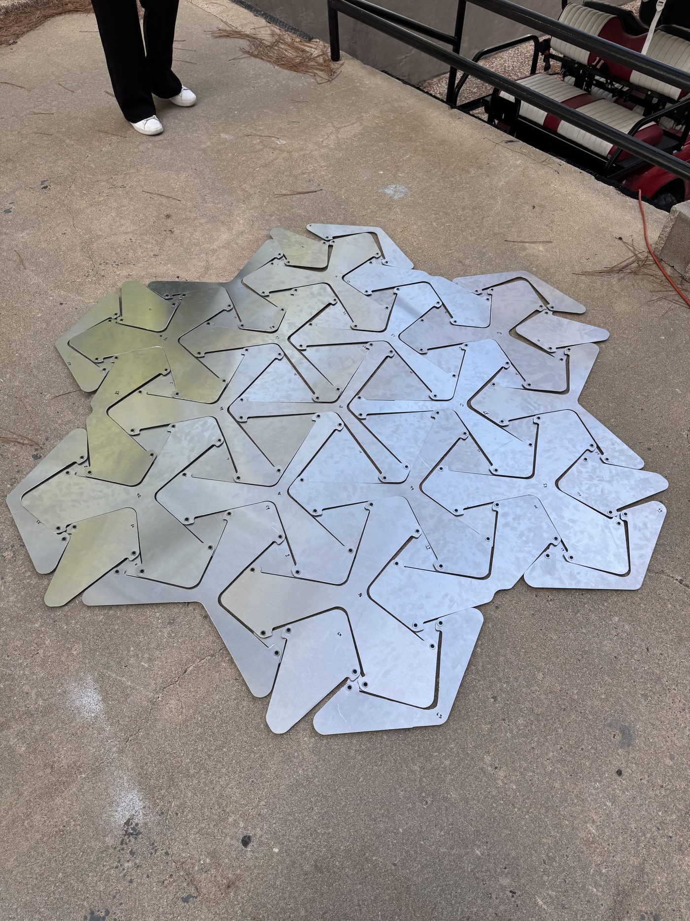 Numbered aluminium plates in the bistable auxetic pattern, riveted at the hinges and laid out flat on a concrete floor