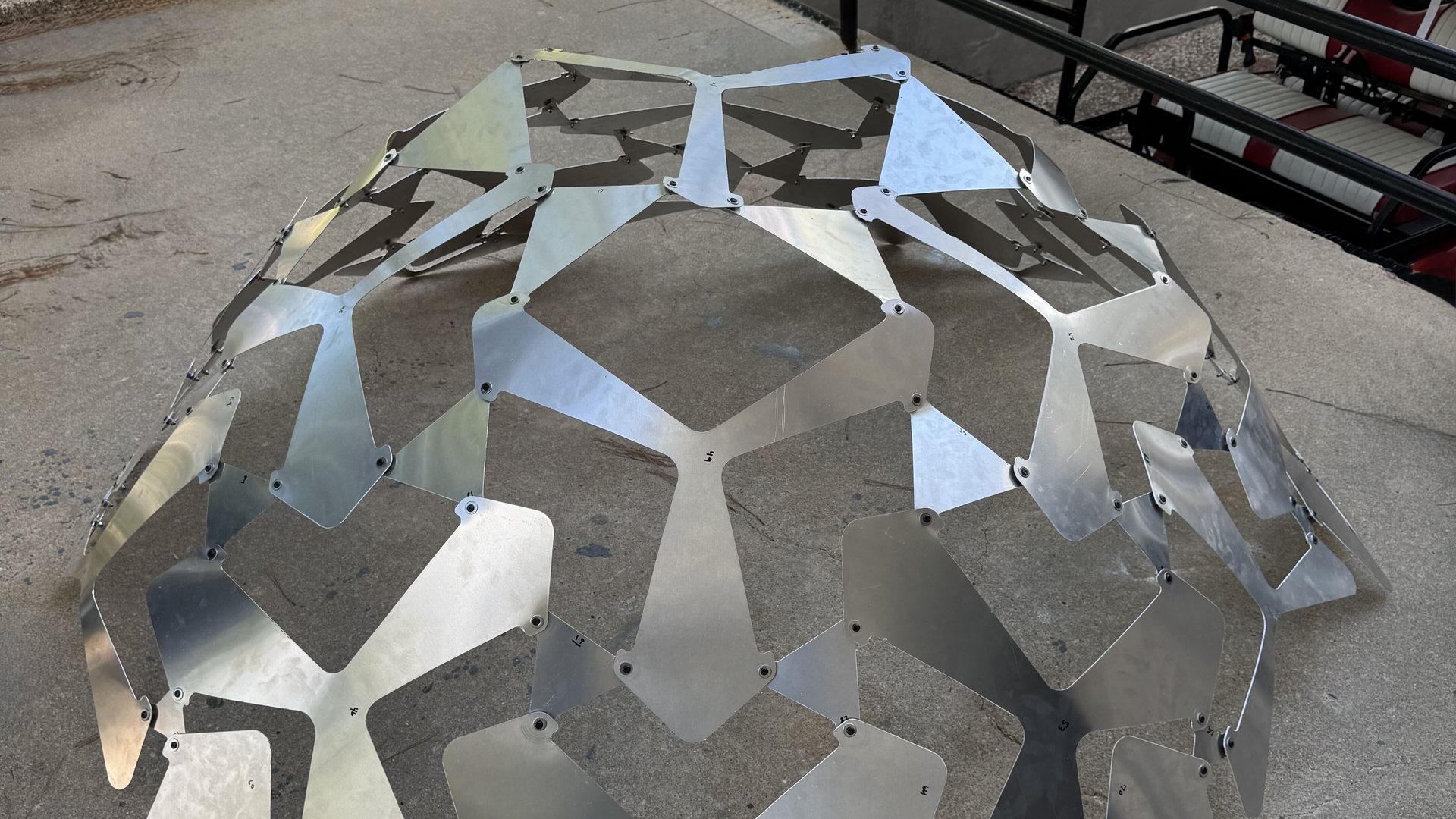 A dome of numbered aluminium plates, joined at the hinges with rivets, standing on a concrete floor